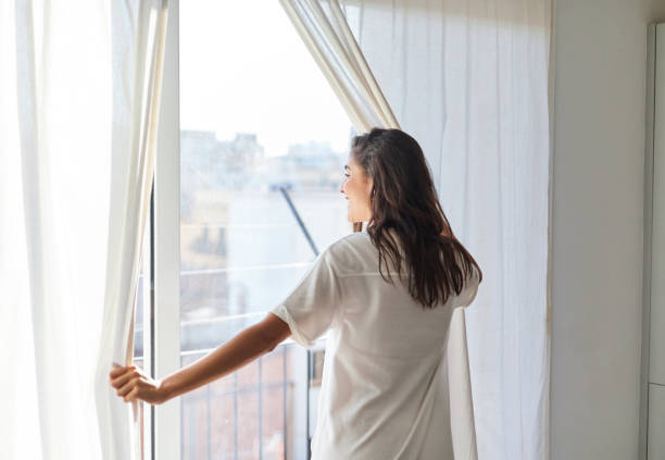 A person standing by a window in morning light, beginning a gentle warm-up movement sequence in their living room